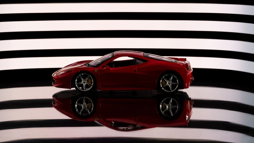 a red toy car sitting on top of a reflective surface, a tilt shift photo, inspired by Hendrick Cornelisz Vroom, photorealism, ferrari 458, on a checkered floor, shutter speed 1/125, dramatic lighting”