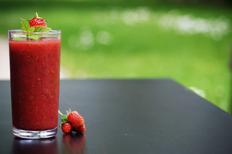 a drink sitting on top of a table next to two strawberries, by Adam Marczyński, pixabay, blender, outdoor photo, highly detailed product photo, istockphoto