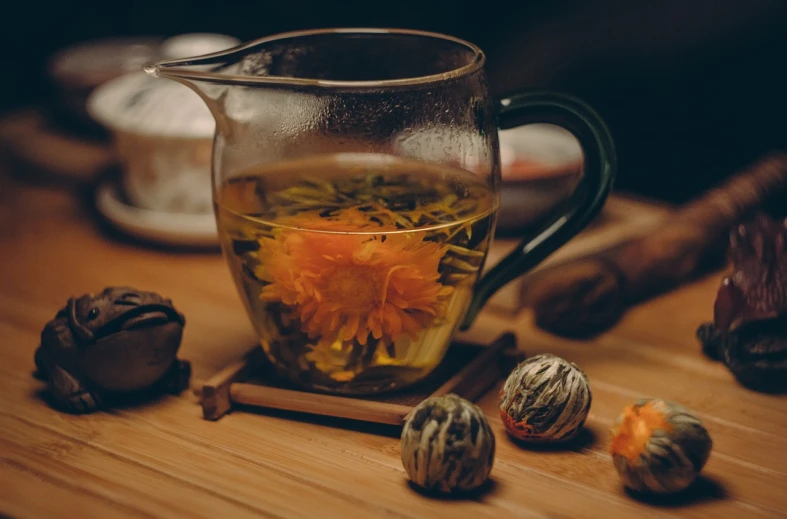 a pitcher filled with flowers sitting on top of a wooden table, pexels, process art, tea ceremony scene, glass jar, lotus, marigold