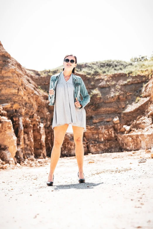 a woman is posing for a picture in the desert, a portrait, figuration libre, rock star, casual summer clothes, legs visible, grey jacket