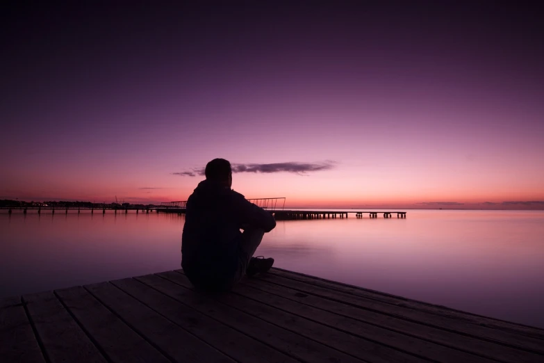 a person sitting on a dock watching the sunset, a picture, by Holger Roed, purple omnious sky, man sitting facing away, self deprecating, photo taken with canon 5d