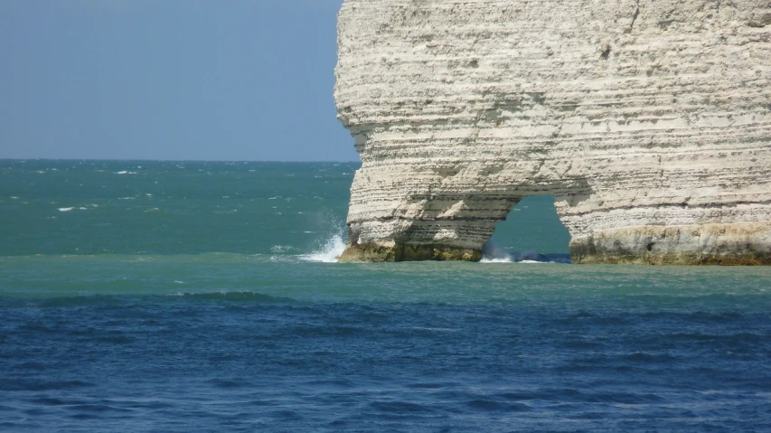 a person riding a surfboard on top of a body of water, a picture, by Edward Corbett, flickr, cliffs of dover, geological strata, archway, paris 2010