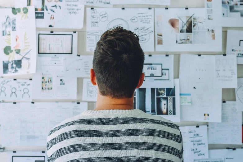 a man standing in front of a wall of papers, pexels, detailed plans and notes, looking from behind, on a canva, 🦑 design