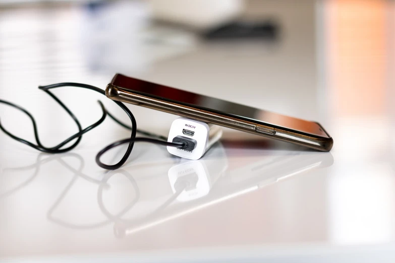 a cell phone sitting on top of a table next to a charger, a picture, by Mathias Kollros, istock, modern very sharp photo, cable plugged in, thin dof