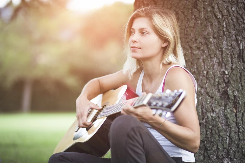 a woman sitting under a tree playing a guitar, shutterstock, blonde women, repetitiveness, 40 years old women, sing with me