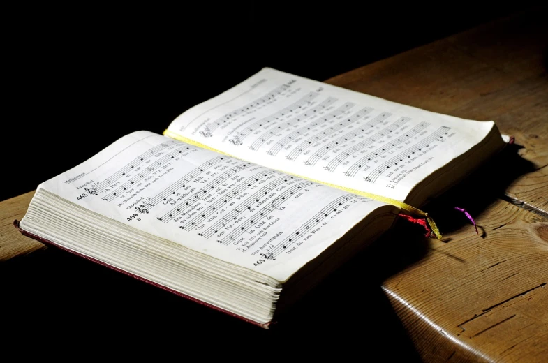 an open book sitting on top of a wooden table, a picture, by Samuel Birmann, pexels, baroque, singing, choir, holy, over-shoulder shot