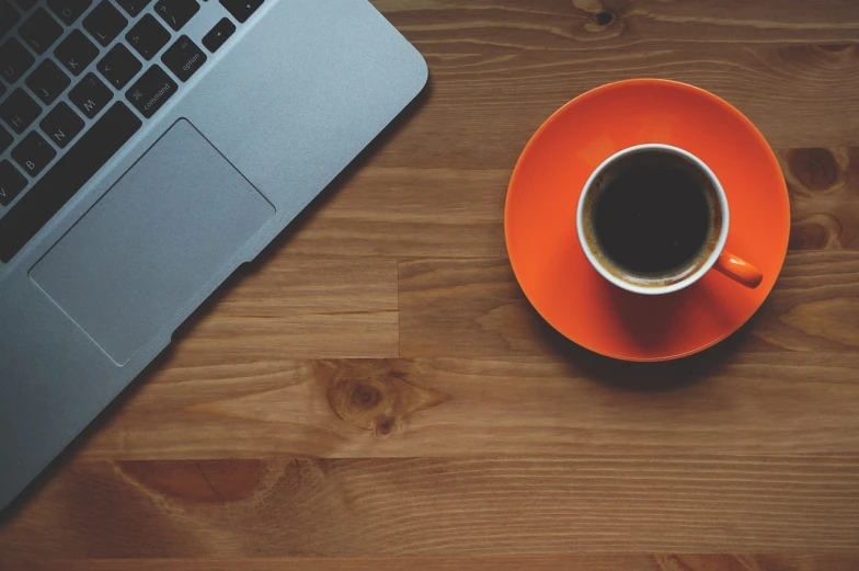 a cup of coffee next to a laptop on a wooden table, by Romain brook, minimalism, orange and black, beautiful wallpaper, banner, tyler west