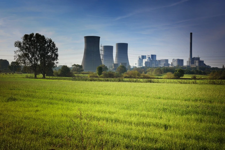 a green field with a power plant in the background, a stock photo, shutterstock, nuclear art, megastructure in the background, 1970s photo