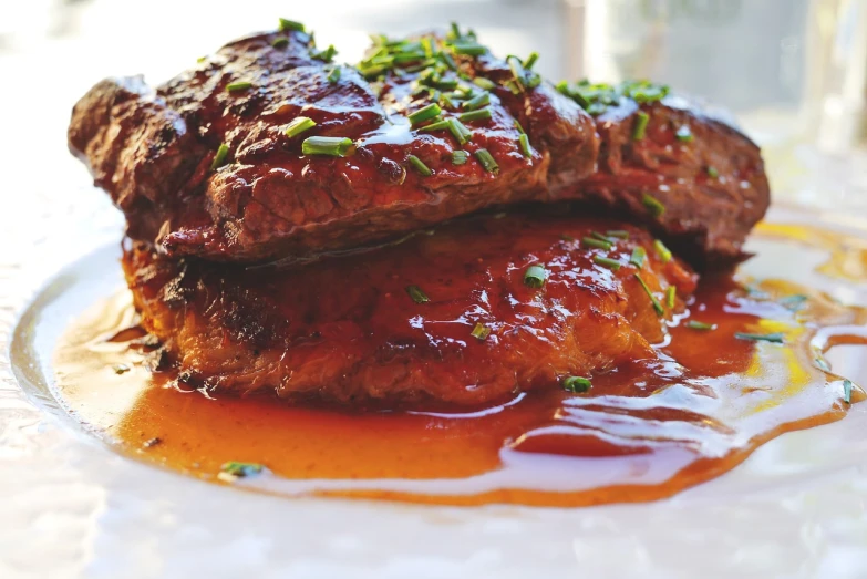 a white plate topped with meat covered in sauce, by Matt Cavotta, pixabay, maple syrup highlights, steak, clover, gooey skin