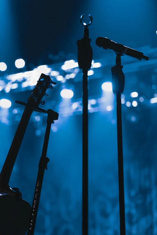 a person holding a guitar in front of a microphone, a picture, shutterstock, concert footage, stanchions, stern blue neon atmosphere, live concert of beyonce