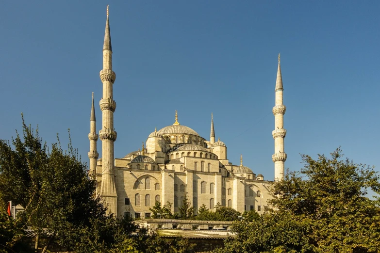 a large white building sitting in the middle of a forest, a picture, inspired by Altoon Sultan, shutterstock, tall stone spires, blue, turkey, dome