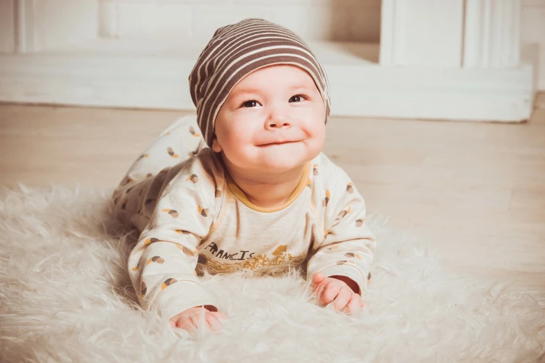 a baby laying on the floor wearing a hat, by Maksimilijan Vanka, pexels, modernism, smiling male, fluffy, avatar image, cutecore