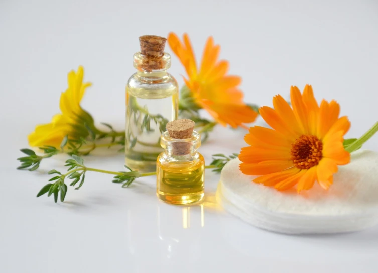 a bottle of essential oil next to some flowers, by Zofia Stryjenska, yellow and orange color scheme, daisy, bottles, soothing