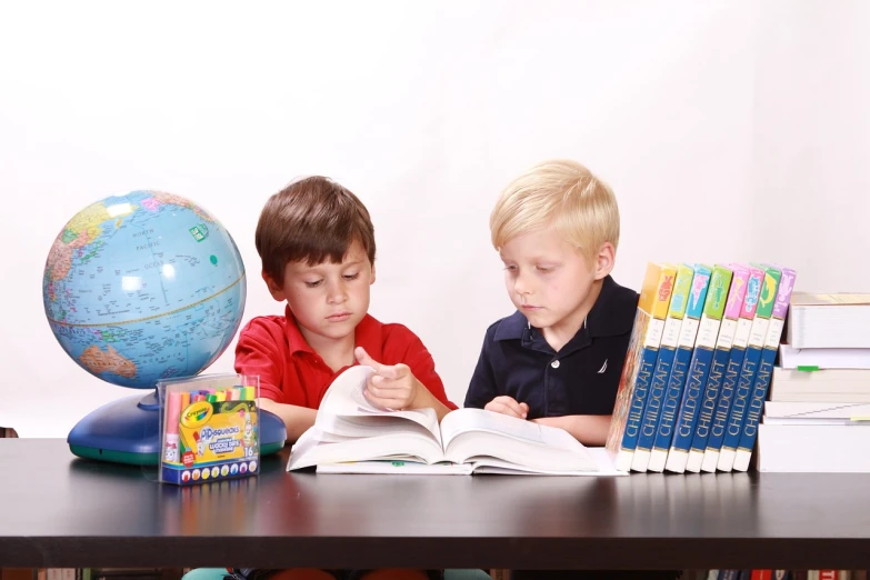 two children sitting at a table reading a book, a photo, high res photo