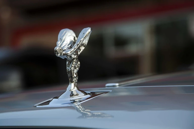 a close up of a hood ornament on a car, an art deco sculpture, by Raymond Normand, pixabay, arabesque, made out of shiny white metal, waving robe movement, in style of chrome hearts, high res