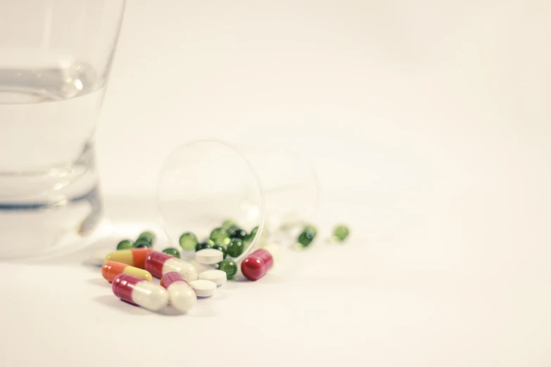 some pills and a glass of water on a table, a tilt shift photo, mouse photo, high res photo, flash photo, product introduction photo