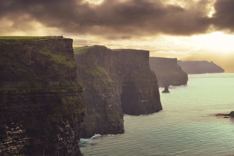 a man standing on top of a cliff next to the ocean, a matte painting, by Andrew Geddes, digital art, ireland, vertical wallpaper, birds flying in the distance, very beautiful photo