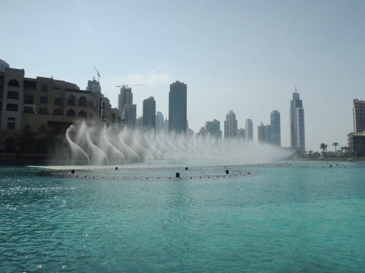 a water fountain in the middle of a large body of water, hurufiyya, dubai, july 2 0 1 1, tourist photo, city morning