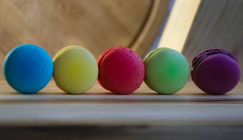 a row of colorful macarons sitting on top of a wooden table, by Thomas Häfner, process art, wine, candy apple, spheres, luminescent colors
