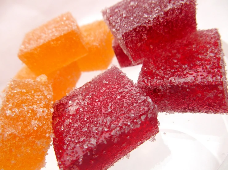 a white plate topped with pieces of fruit covered in sugar, a macro photograph, pexels, crystal cubism, jelly - like texture, red and orange colored, cube shaped, cane