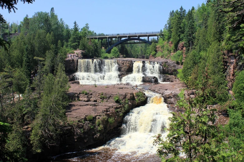 a waterfall with a bridge in the background, by Jim Nelson, superior look, on a bright day, multiple waterfalls, well preserved