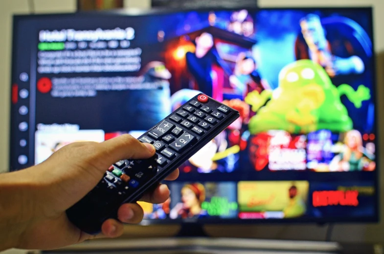 a person holding a remote control in front of a television, a cartoon, by Dan Content, pexels, netflix, large commercial led screens, voitv, blue rays from tv