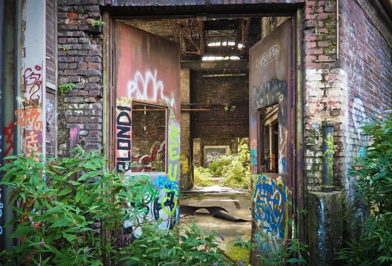 an abandoned building with graffiti all over it, by Arnie Swekel, flickr, graffiti, overgrown jungle ruins, open door, factories and nature, entrance to abandoned mine