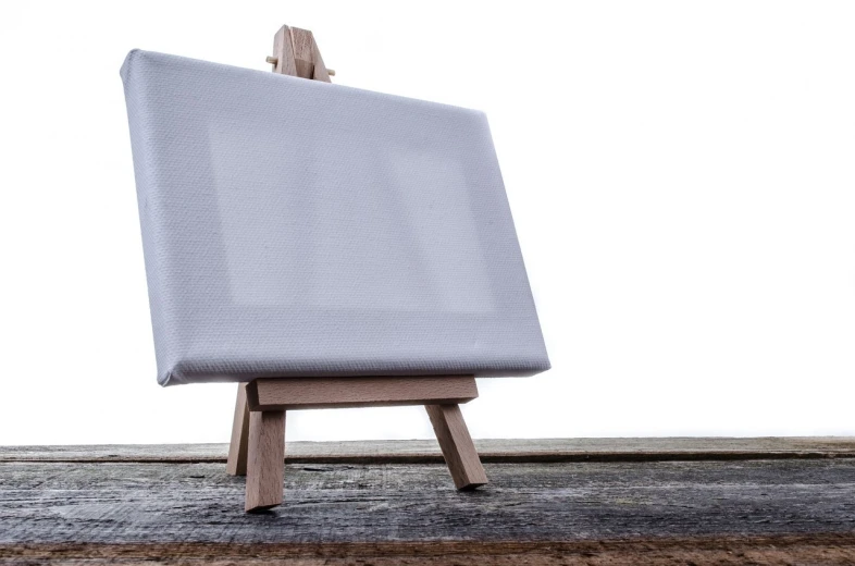 an easel sitting on top of a wooden table, a minimalist painting, inspired by Art Brenner, pixabay, arbeitsrat für kunst, white canvas background, portrait of a small, airbrush on canvas, packshot