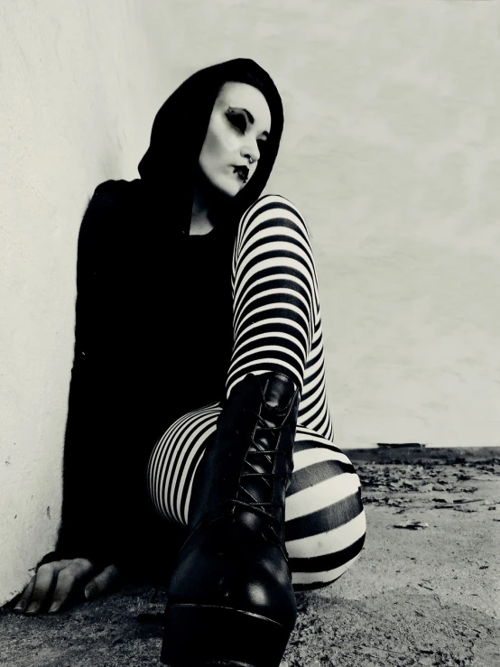 a black and white photo of a woman sitting on the ground, a black and white photo, gothic art, stripey pants, emo makeup, desktop wallpaper, wearing dark maritime clothing