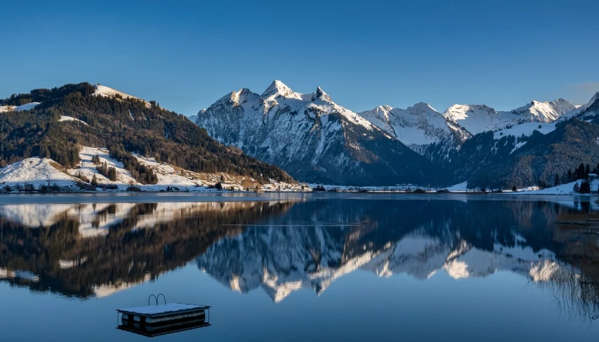 a large body of water surrounded by snow covered mountains, a picture, by Karl Walser, flickr, precisionism, beautiful rtx reflections, early morning mood, clear blue skies, lpoty