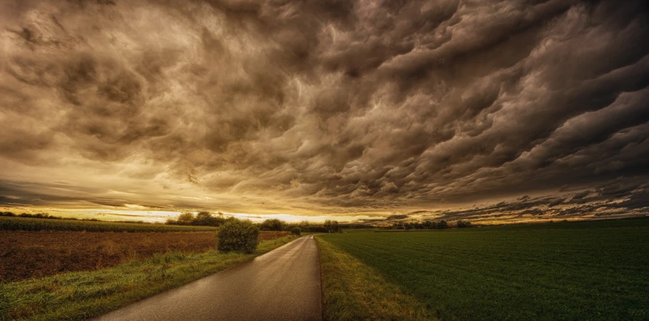 a road in the middle of a field under a cloudy sky, a picture, by Jozef Czapski, renaissance, dark mammatus cloud, highly turbulent, golden clouds, gloomy mood. greg rutkowski