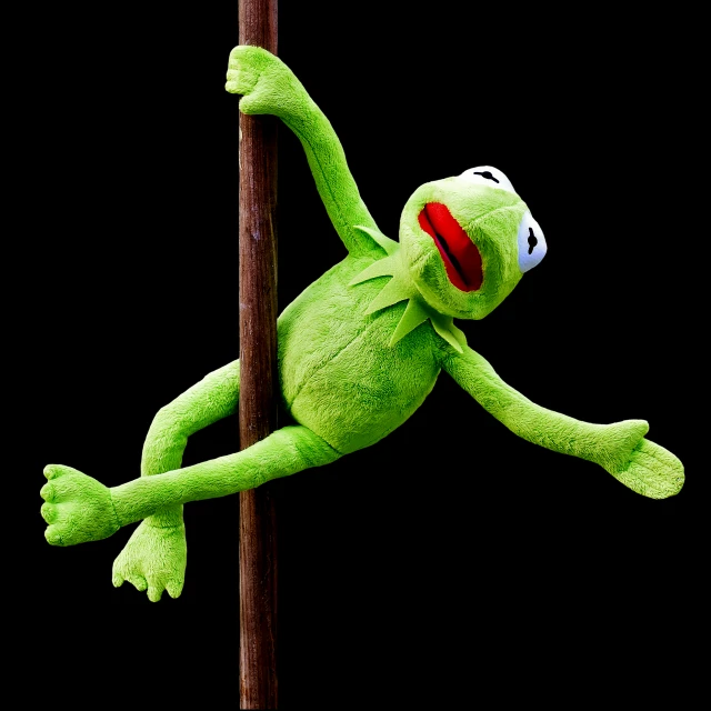 a green stuffed animal hanging from a pole, by Hans Schwarz, kermit, acrobatic pose, on a black background, laugh