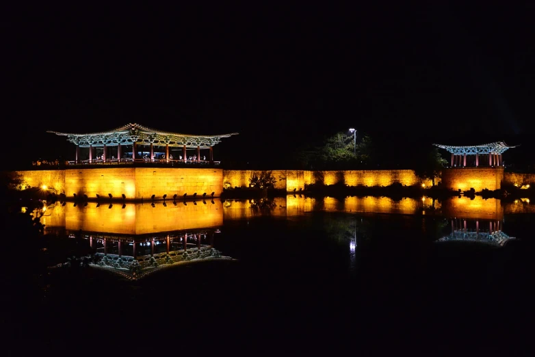 a large building sitting on top of a lake at night, by Yi Jaegwan, flickr, sōsaku hanga, korean traditional palace, bhutan, panoramic, reflection of led lights