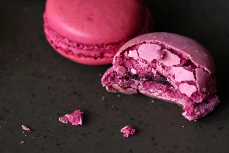 a pink macaron with a bite taken out of it, a macro photograph, inspired by François Louis Thomas Francia, pexels, baroque, almost black, very smoky paris bar, mangosteen, crimson - black beehive