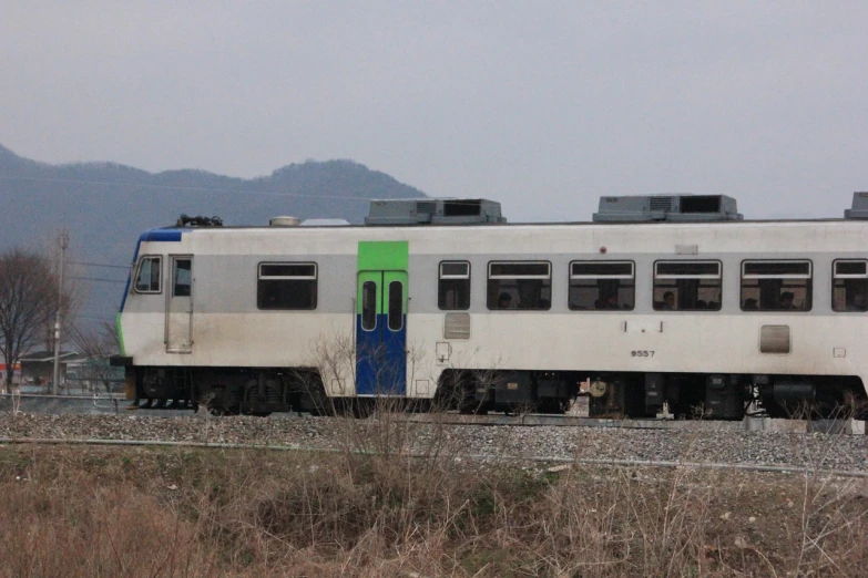 a train on a train track with mountains in the background, flickr, sōsaku hanga, camouflage scheme, very symmetrical body, saitama prefecture, 3/4 side view