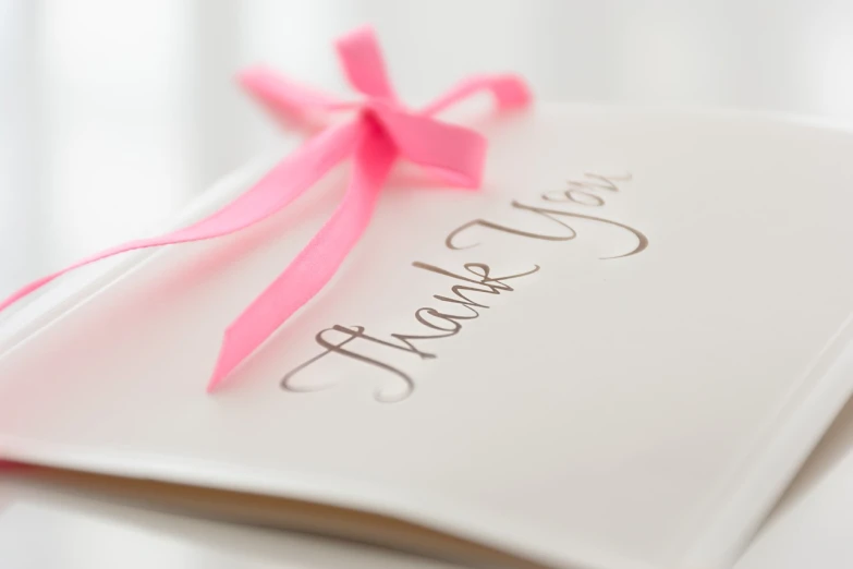 a thank card with a pink ribbon tied to it, professional closeup photo, letters, thin, highly stylized