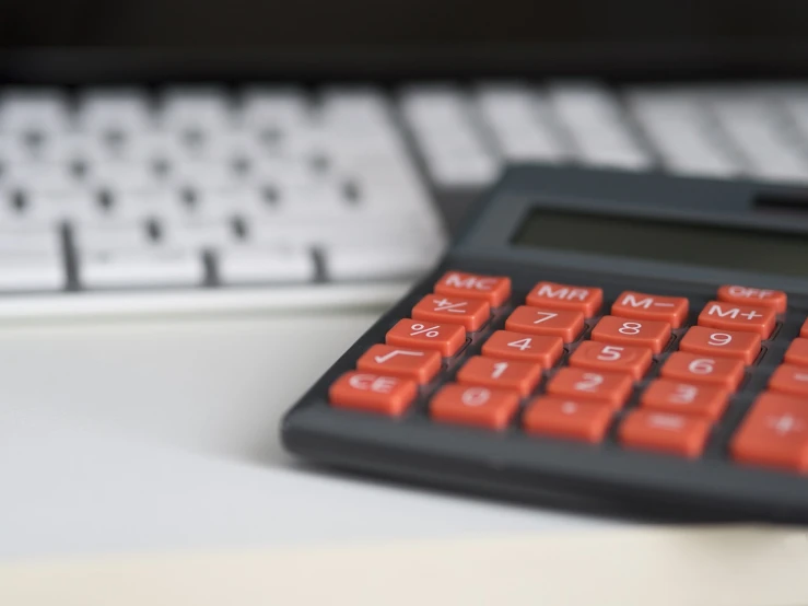 a calculator sitting on a desk next to a keyboard, by Steven Belledin, red brown and grey color scheme, closeup photo, black and orange colour palette, file photo