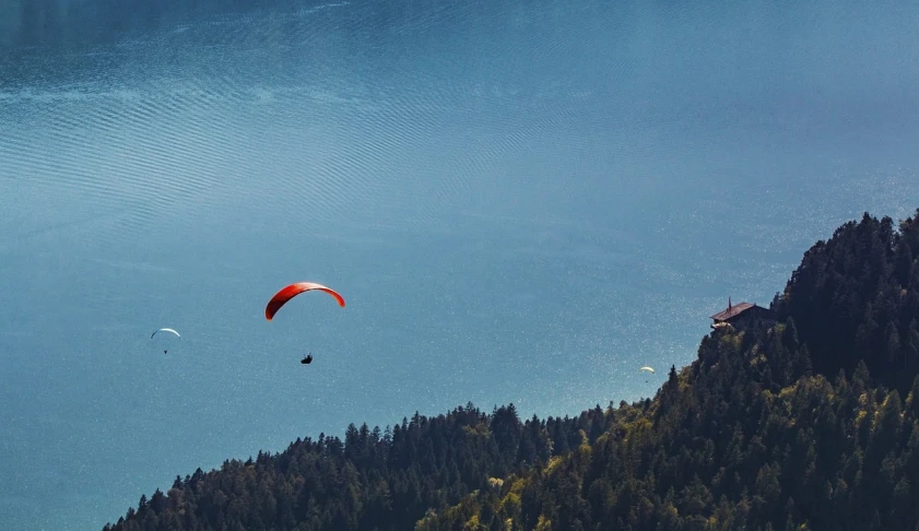 a paraglider flying over a large body of water, a picture, by Werner Gutzeit, pexels, figuration libre, telephoto long distance shot, lakeside, guillaume tholly, istock