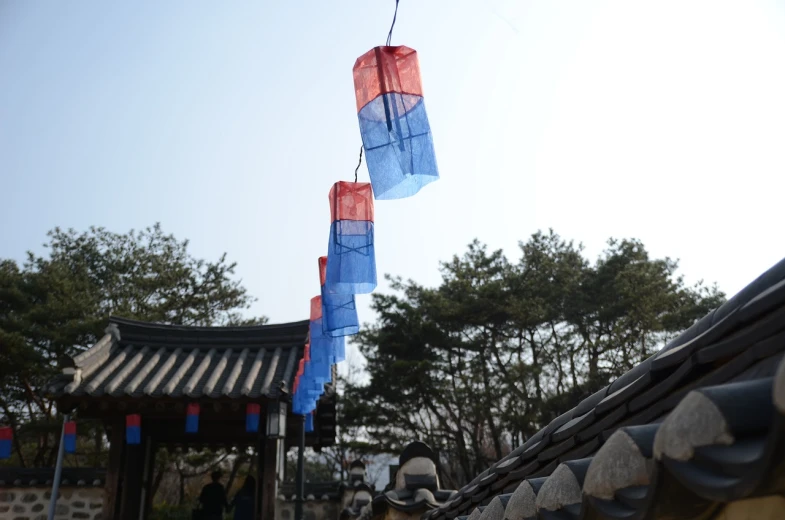 a couple of kites hanging from the side of a building, inspired by Kim Hong-do, dau-al-set, hanging lanterns, blue and red color scheme, nice spring afternoon lighting, flag