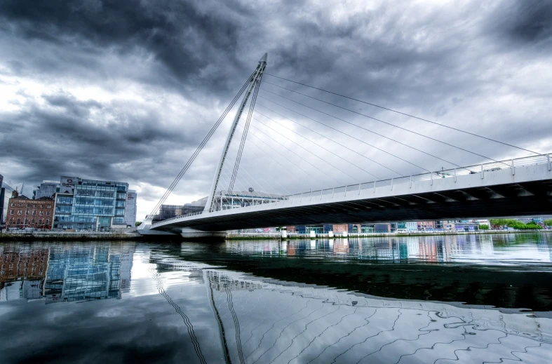 a bridge over a body of water under a cloudy sky, by Eamon Everall, flickr, reflections on wet streets, modern high sharpness photo, twisted waterway, dramatic architecture