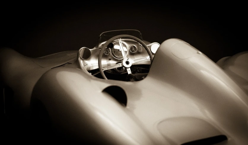 a black and white photo of a sports car, a portrait, inspired by Jerry Schatzberg, retrofuturism, single steering wheel, sepia toned, toy photography, f1.2