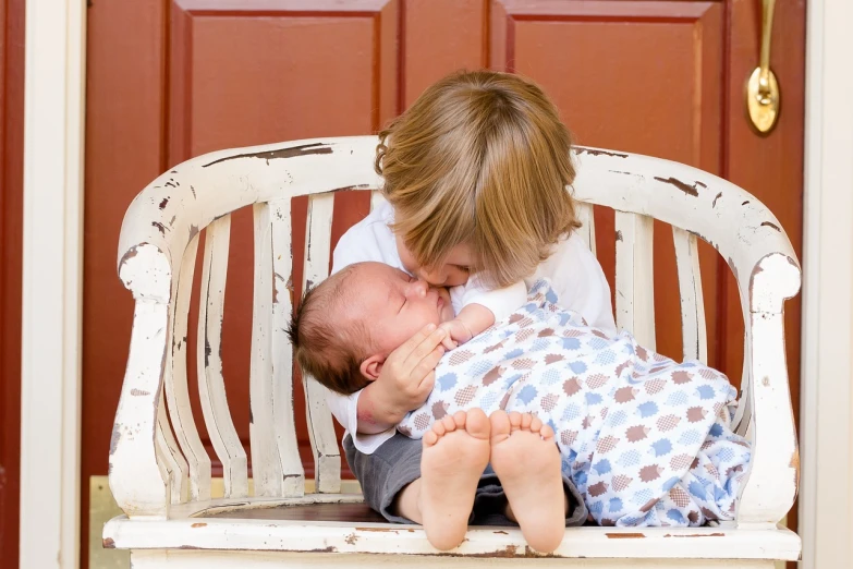 a woman kissing a baby on top of a white bench, a picture, by Robert Medley, pixabay, incoherents, they are siblings, little brother, boys, asleep