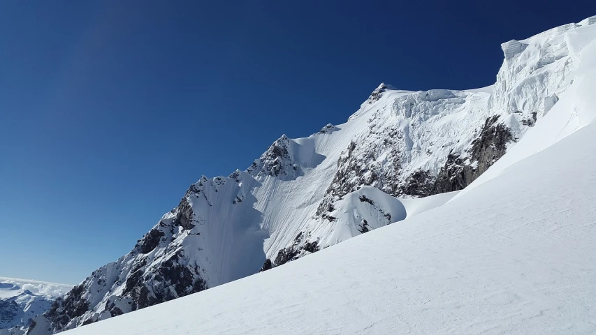 a man riding skis down the side of a snow covered slope, a picture, by Peter Churcher, flickr, les nabis, clear blue skies, giant imposing mountain, very detailed curve, seen from afar