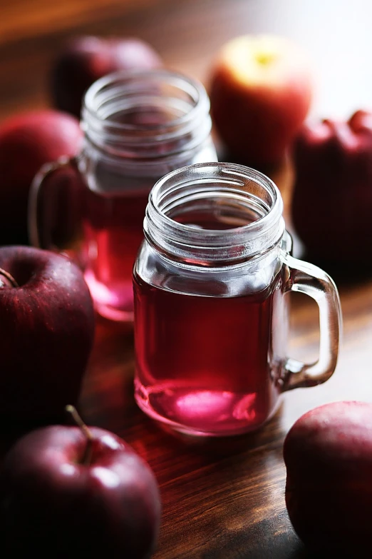 a group of apples sitting on top of a wooden table, a stock photo, shutterstock, berry juice, glass jar, purple and red colors, close up food photography