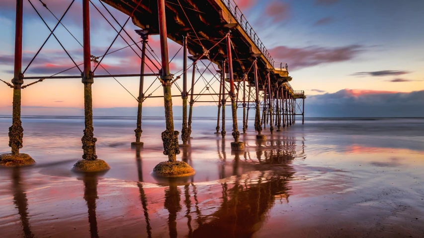 a pier sitting on top of a sandy beach, a picture, inspired by George Pirie, shutterstock, romanticism, neon reflections in the puddles, industrial colours, yorkshire, amazing details