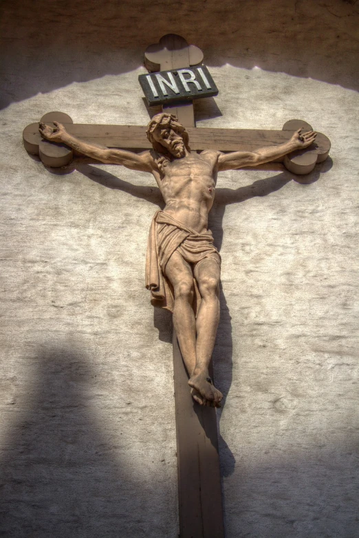 a statue of jesus hanging on the side of a building, a statue, by Hans Schwarz, shutterstock, crucifix, highly detailed hdr, wooden, 33mm photo