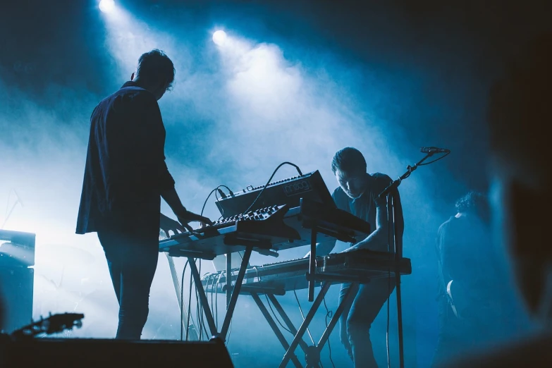 a couple of people that are standing in front of a keyboard, a picture, by Matija Jama, concert footage, blueish tones, they are crouching, hammershøi