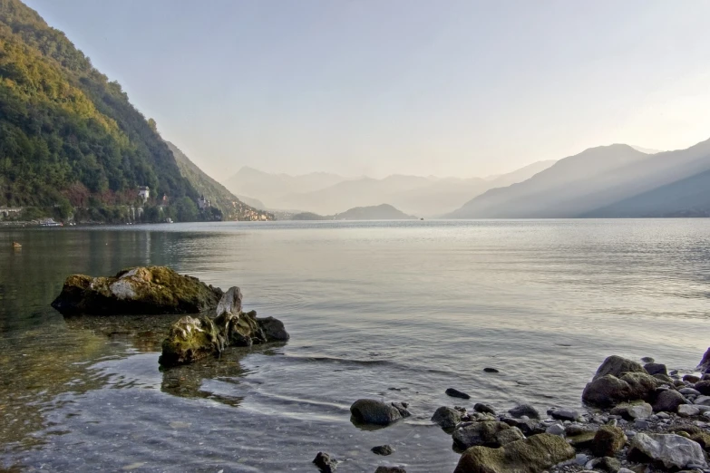 a person sitting on a rock next to a body of water, a picture, by Rudolf Schlichter, flickr, beach is between the two valleys, abbondio stazio, soft morning light, hdr on