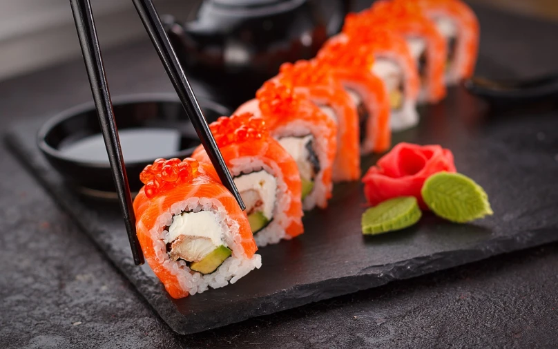 a black plate topped with sushi and chopsticks, a picture, inspired by Maki Haku, shutterstock, avatar image, professional food photography, orange fluffy spines, 🦩🪐🐞👩🏻🦳