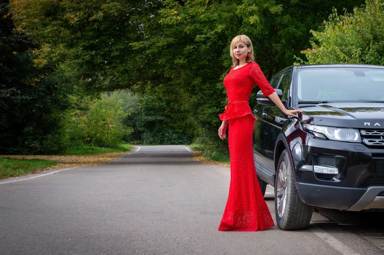 a woman in a red dress standing next to a black car, inspired by Leila Faithfull, shutterstock, very accurate photo, elegant glamourous cosplay, outdoor photo, award-winning very detailed